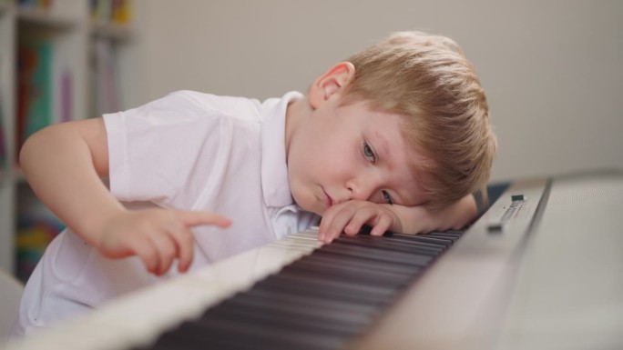 疲惫的男孩躺在地上，胡乱地按着电子钢琴上的键