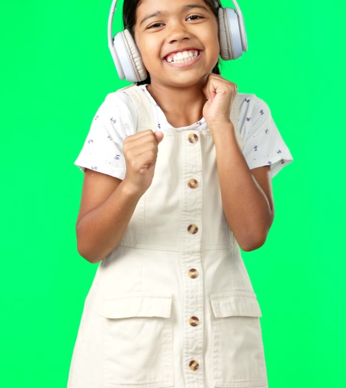 孩子们，音乐和舞蹈与一个女孩在一个绿色的屏幕背景在演播室流式音频耳机。肖像，微笑和乐趣与一个可爱的小
