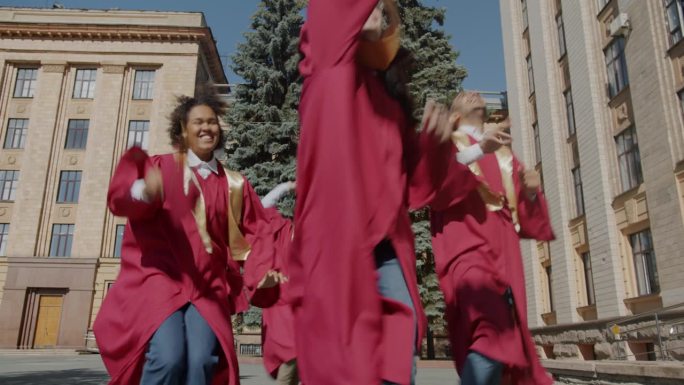 多民族学生在大学校园里奔跑，扔帽子表达毕业那天的快乐