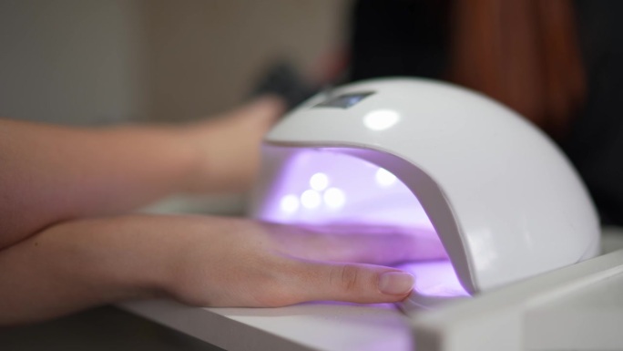 在美容院，一个女人把手伸进紫外线灯里做指甲的特写
