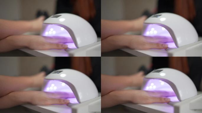 在美容院，一个女人把手伸进紫外线灯里做指甲的特写