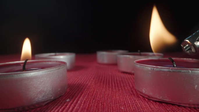 我轮流点燃红色桌布上的红色蜡烛。极端特写镜头。