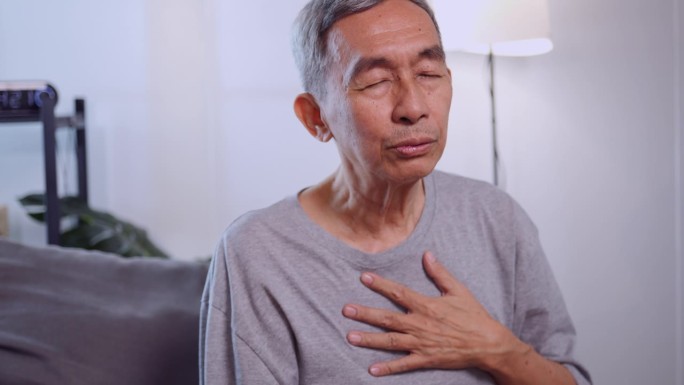 一位亚洲老人坐在家里的沙发上呼吸困难。