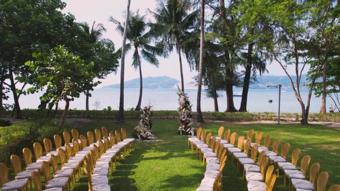 空中无人机俯瞰婚礼拱门和海滩附近花园的椅子。在绿色草坪上装饰的婚礼。晴朗的夏天。美丽的婚礼装饰在夏日