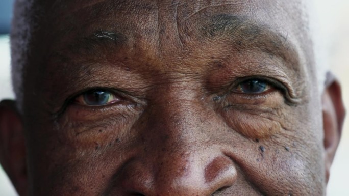 一个黑人老人闭上眼睛沉思，一个非洲裔老人沉思的微距特写，睁开眼睛盯着镜头微笑