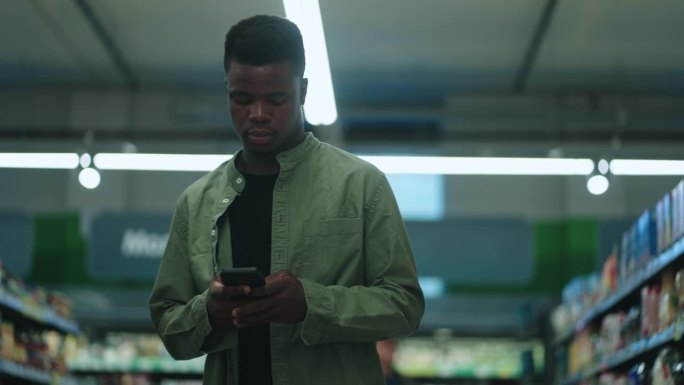 一名黑人男子在杂货店浏览新鲜农产品，用智能手机寻找最优惠的健康食品