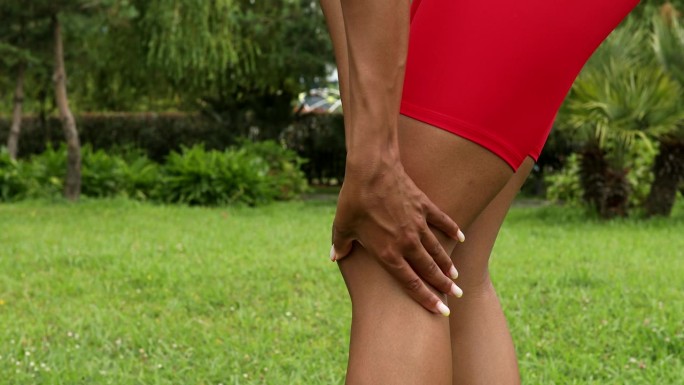 肌肉疼痛的非裔美国跑步运动员。黑人女性在户外慢跑时按摩伸展，受伤。
