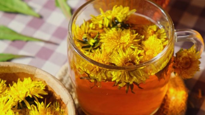 蒲公英花健康茶在玻璃茶壶和玻璃杯子在桌子上。夏日花园附近，从家中新鲜的蒲公英花中倒出美味的凉茶。热蒲