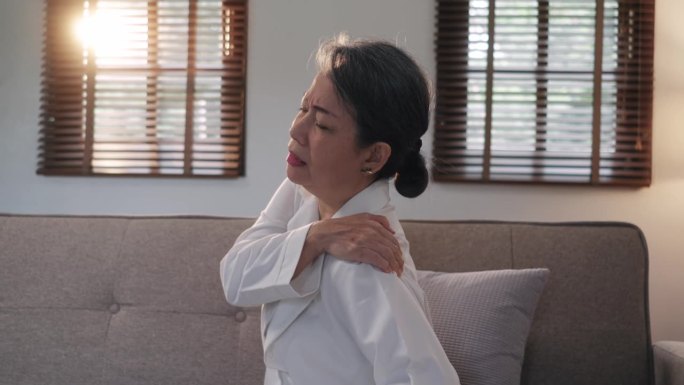 老妇人在按摩肩膀，缓解疼痛。关节疼痛概念。