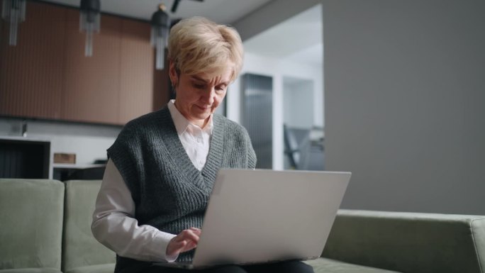 活跃的退休妇女在家远程工作，老太太的肖像，膝上放着笔记本电脑