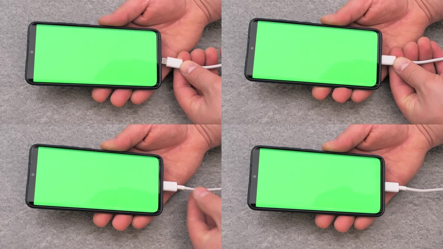 充电给手机、智能手机充电。一个男人手里拿着一部手机。连接USB充电器。设备充电过程。绿色的屏幕。