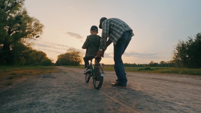 孙子和爷爷一起学在户外骑自行车。
