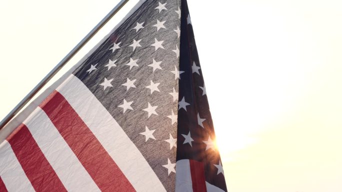 近距离挥舞着美国国旗在自然户外设置与太阳射线耀斑自然户外背景。七月四日，独立日，七月四日，阵亡将士纪