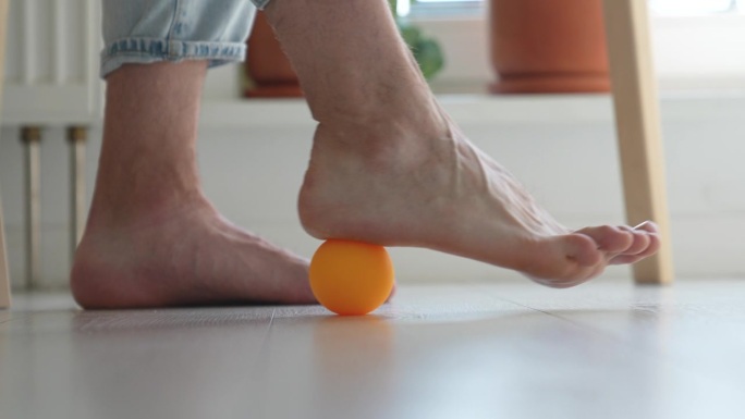 在长时间久坐不动的工作中，男子在桌子下使用硅胶球进行足部按摩。