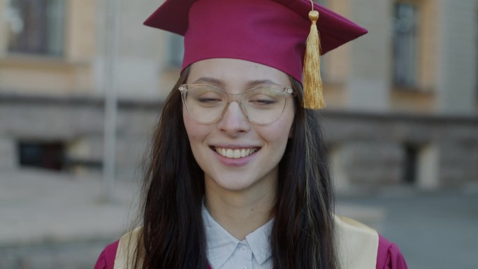 成功的年轻女子从大学毕业的肖像站在校园里穿着长袍和帽子