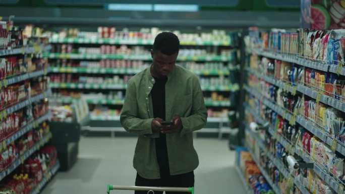 一名非裔美国人在超市购买健康食品，使用数字设备比较价格并进行购买