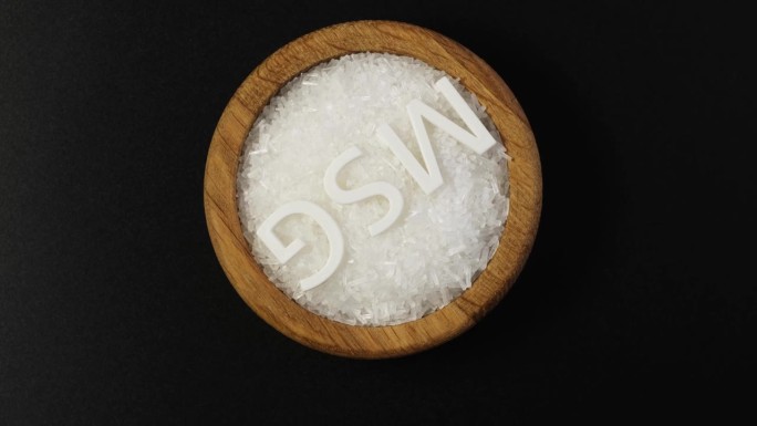 谷氨酸钠，白色结晶颗粒装在木碗中，符号MSG，旋转。食品添加剂E621，又称中国盐或五味、鲜味。天然