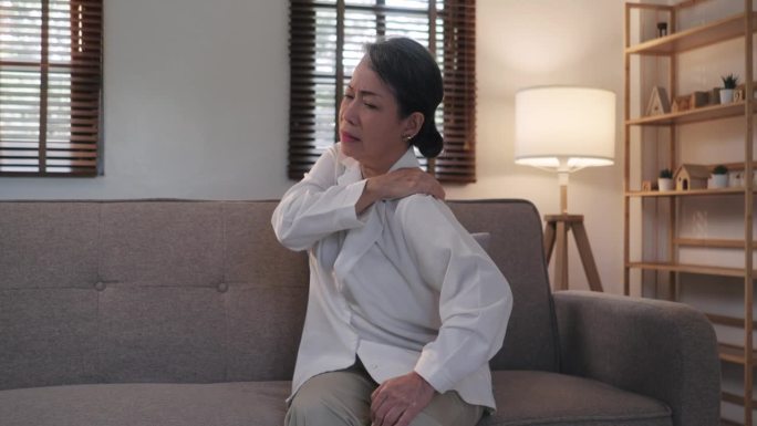 老妇人在按摩肩膀，缓解疼痛。关节疼痛概念。