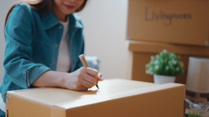 亚洲妇女在打包搬家时在箱子上贴上标签