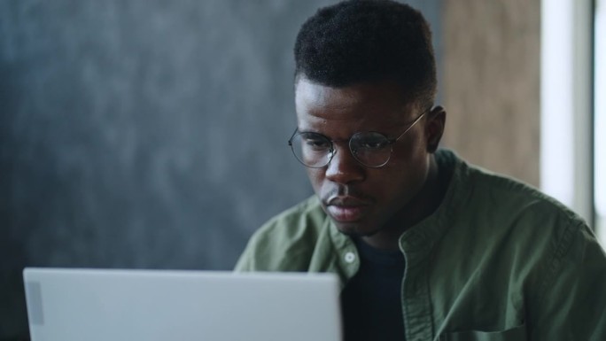 一位深思熟虑的年轻非裔美国创业公司创始人坐在咖啡馆的办公桌前，在笔记本电脑上寻找创新的商业解决方案，
