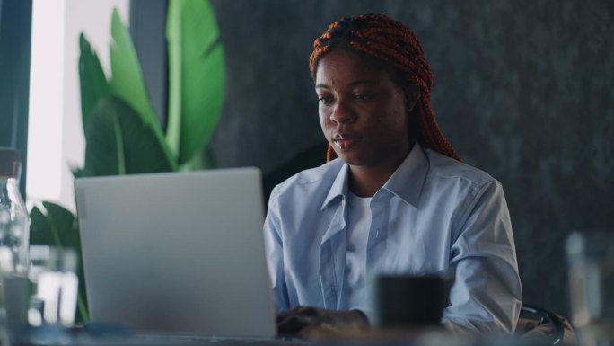 高效的远程工作:一名黑人女性一边在舒适的咖啡馆里喝着咖啡，一边在笔记本电脑上打字