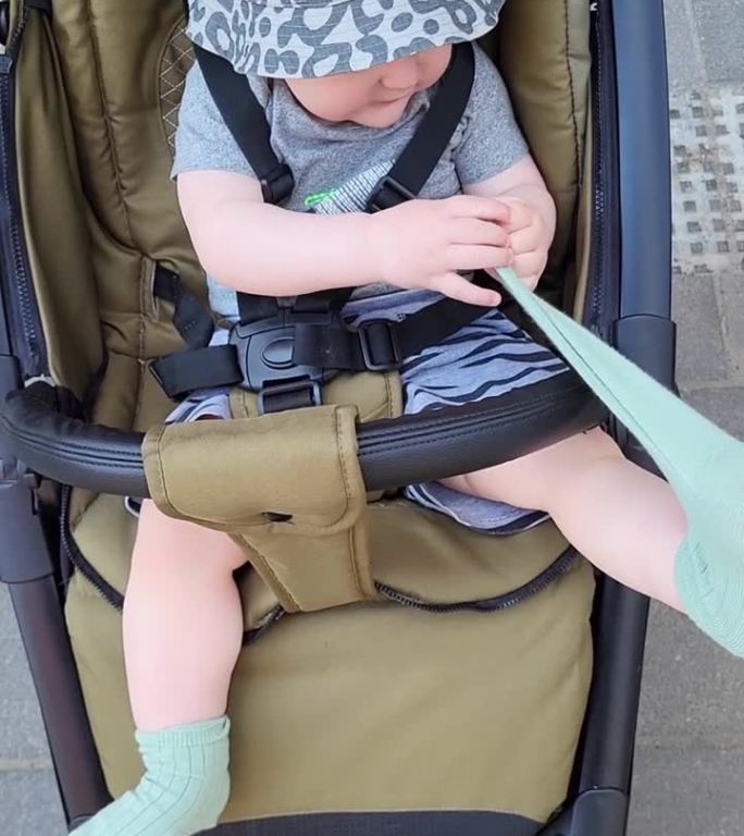 蹒跚学步的小男孩脱下衣服。这个孩子坐在婴儿车里拒绝穿袜子和脱衣服。1岁左右(11个月)