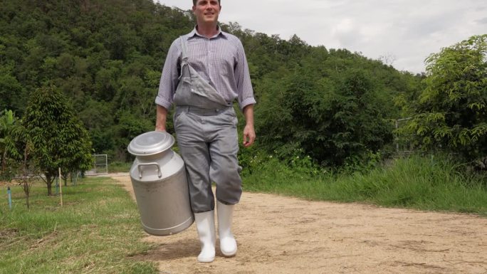 一个男奶农拿着一个大牛奶罐走在农场外面
