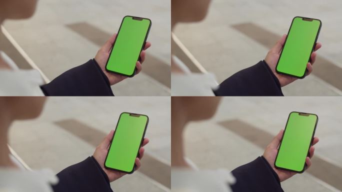 在城市的街道上使用绿色色度键屏的智能手机的妇女。