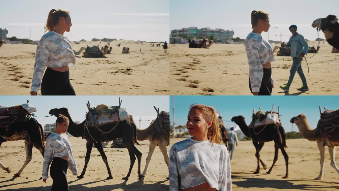女游客在沙滩上走在骆驼旁边