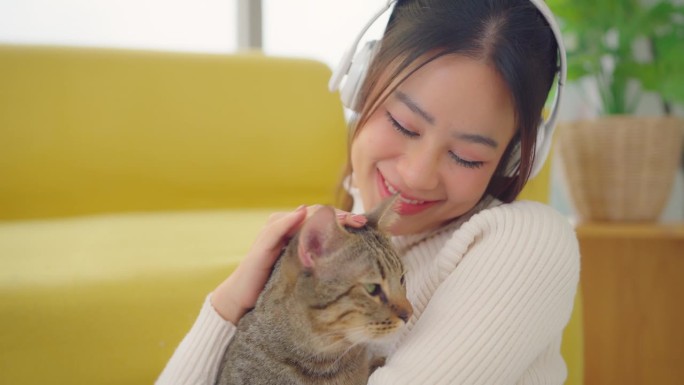 美丽的女人戴着耳机和她的猫玩回家。