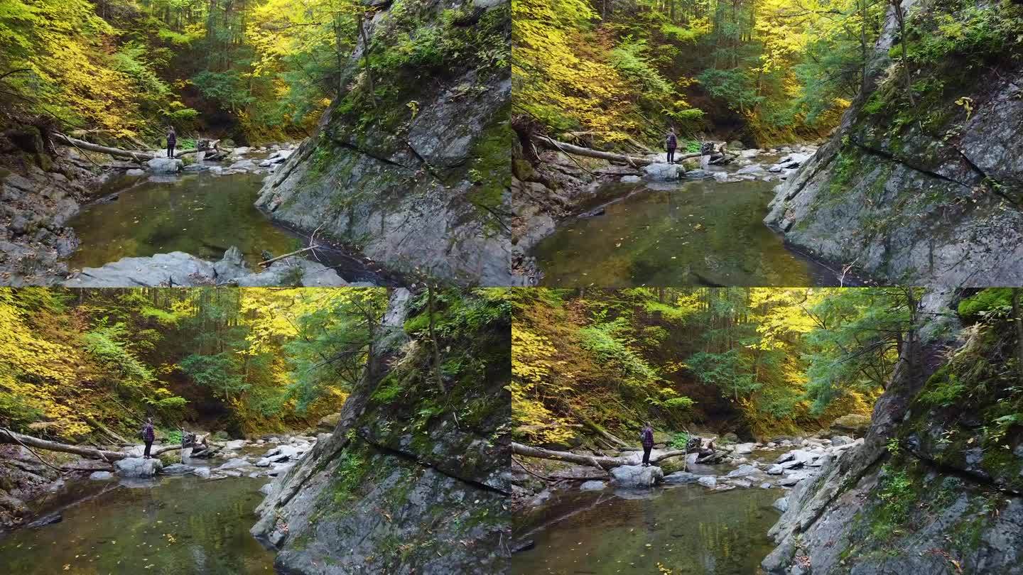 空中拍向徒步旅行者过河的巨石空中拍在令人惊叹的秋天峡谷苔藓和树叶