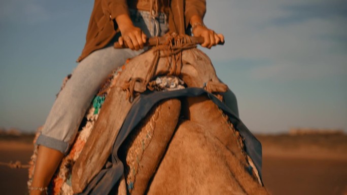 慢镜头:在多云的天空下骑骆驼的女游客