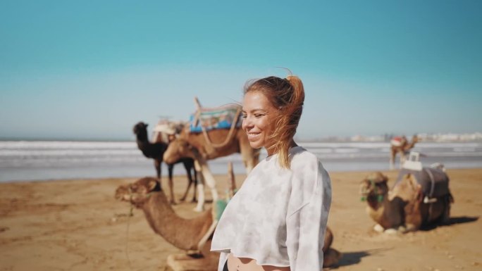 女游客在沙滩上散步，骆驼在沙滩上休息