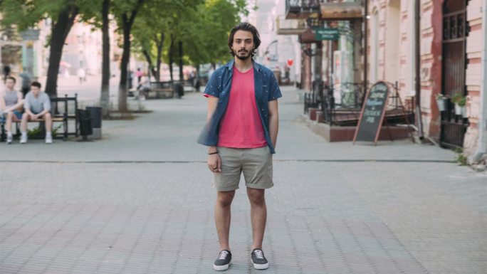 延时拍摄的年轻阿拉伯男子站在市中心的街道上，看着相机