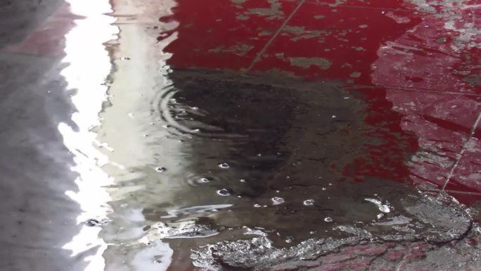 人的脚与聚集在红色地板上的雨水玩耍的特写镜头，高清镜头。在水坑里玩得开心。