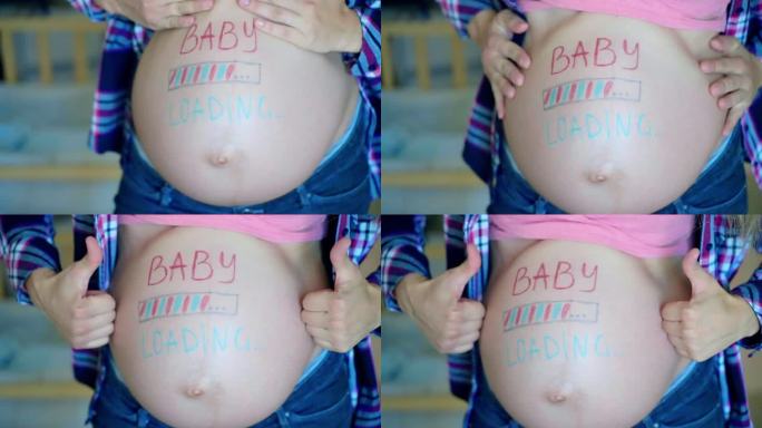 蓝粉相间的婴儿在孕妇的肚子上写着铭文，期待着妈妈等待孩子的到来，快乐的女性慢慢地在镜头前摆姿势，竖起