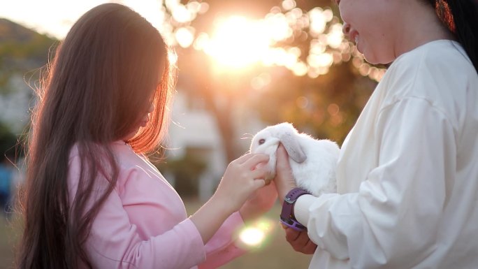 可爱的妈妈和女儿在他们的怀抱中享受着可爱的兔子。