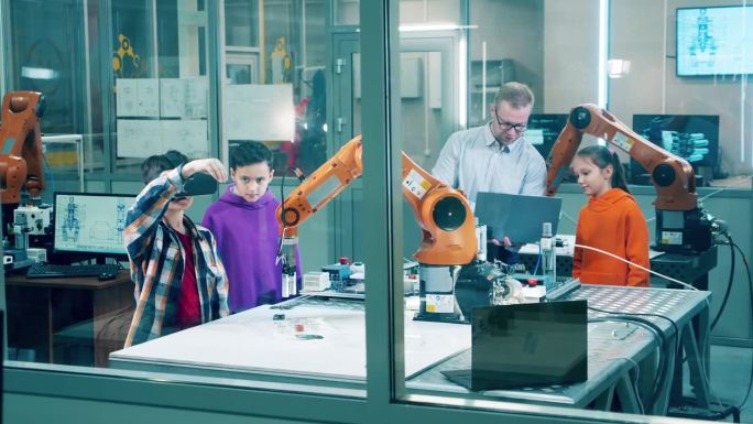 在一个现代化的学校实验室里，一群孩子正在使用虚拟现实技术来管理机器人