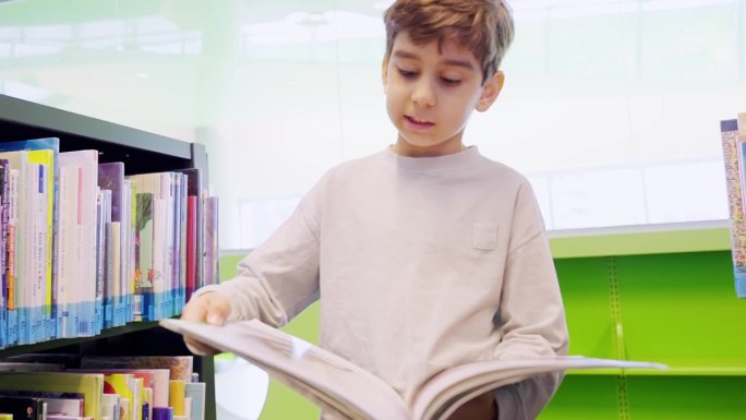 可爱的白人小男孩在图书馆的书架旁看书。