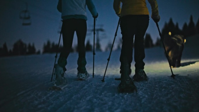 黄昏时分，人们在滑雪胜地的雪坡上穿雪鞋
