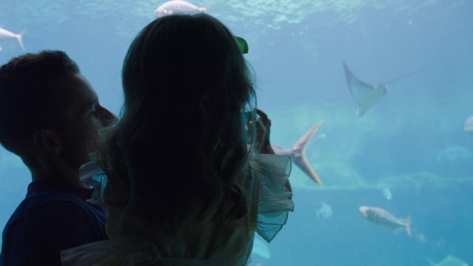父亲和女儿用手机相机拍摄海洋生物在鱼缸里游泳，在海洋馆玩得很开心，分享在社交媒体上