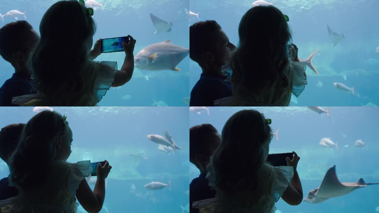 父亲和女儿用手机相机拍摄海洋生物在鱼缸里游泳，在海洋馆玩得很开心，分享在社交媒体上