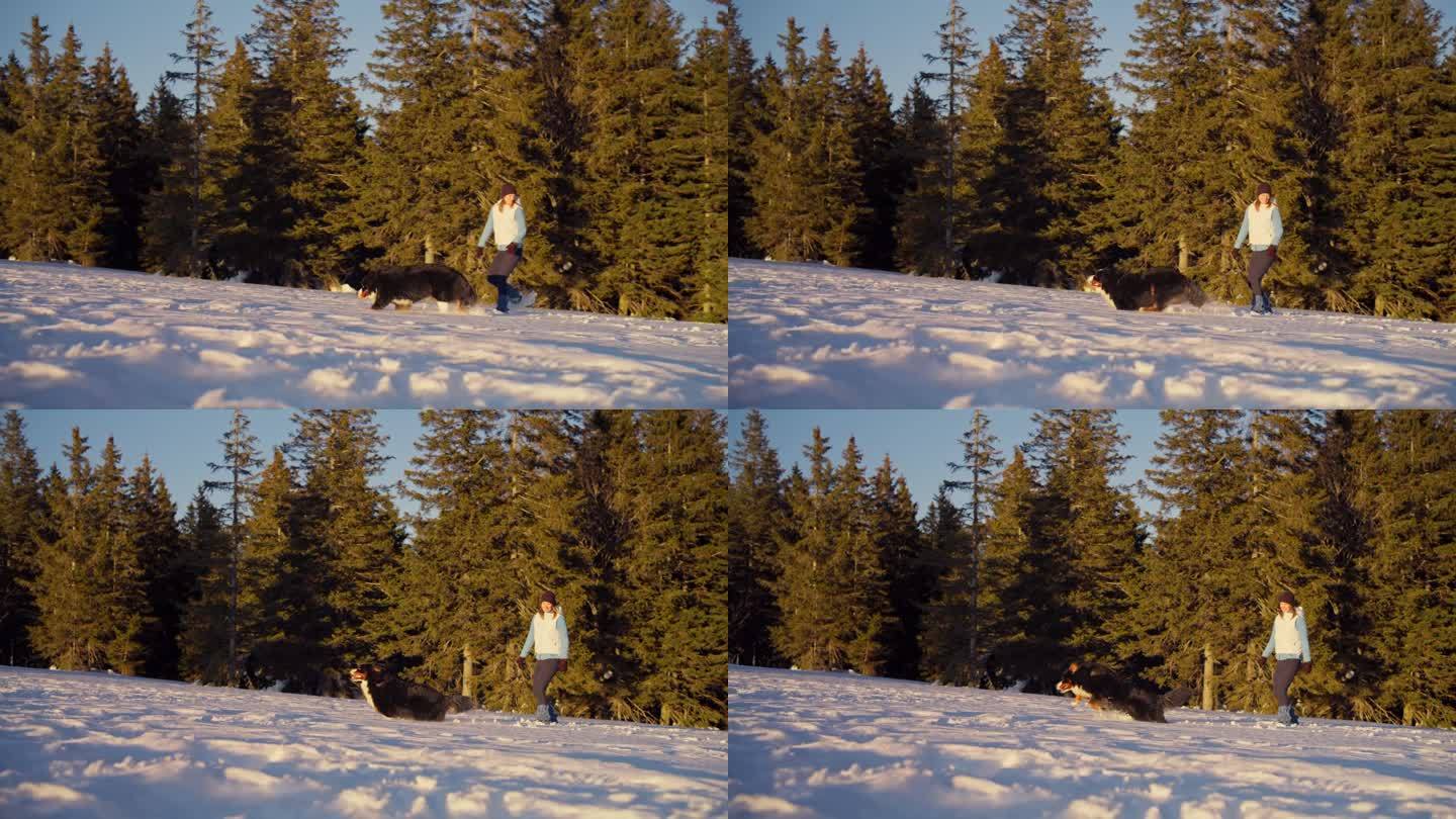 一名女子穿着雪鞋在雪地上行走，她的狗在她身边奔跑