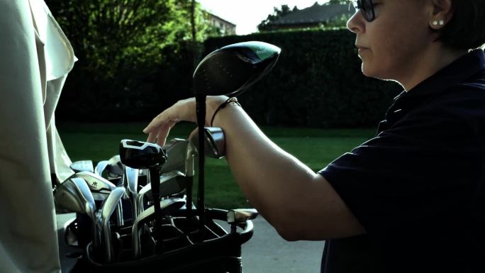 在一个阳光明媚的日子里，高尔夫球手从高尔夫球袋里拿起一个带有镜头光圈的高尔夫球杆