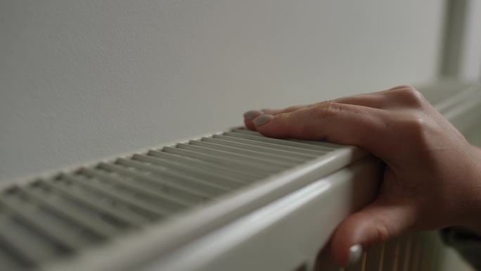 特写:女性白种人的手摸着暖气片检查家里的温度。不认识的女人和暖气装置在室内。
