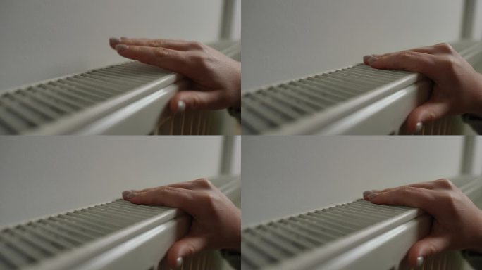 特写:女性白种人的手摸着暖气片检查家里的温度。不认识的女人和暖气装置在室内。