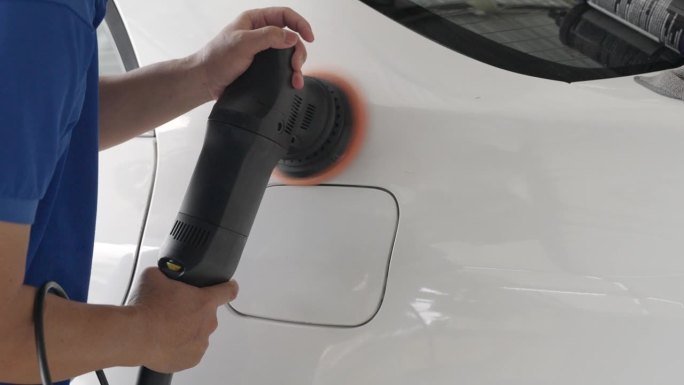 近距离拍摄一位使用电动汽车打蜡机给汽车打蜡的男子的手