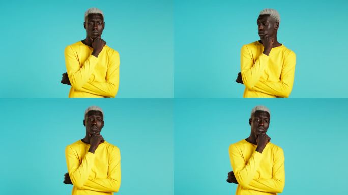 在蓝色背景下，一个非洲人抬头环顾四周。忧虑沉思的表情。穿着黄色t恤的帅气男模特