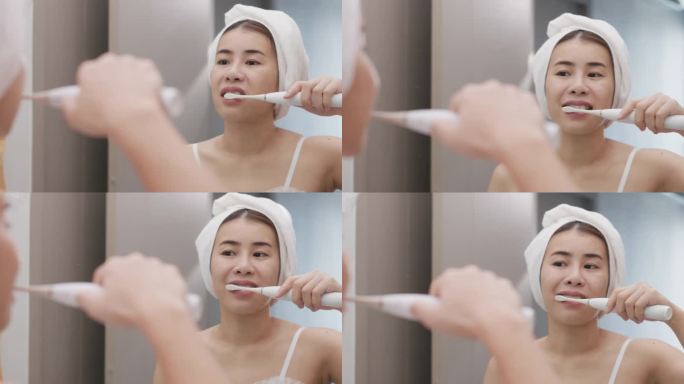 美丽的亚洲女人在浴室的镜子旁刷牙