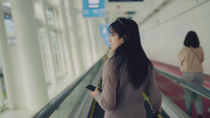 一名亚洲妇女在候机楼准备继续她的旅程。她站在人行道上望着天空